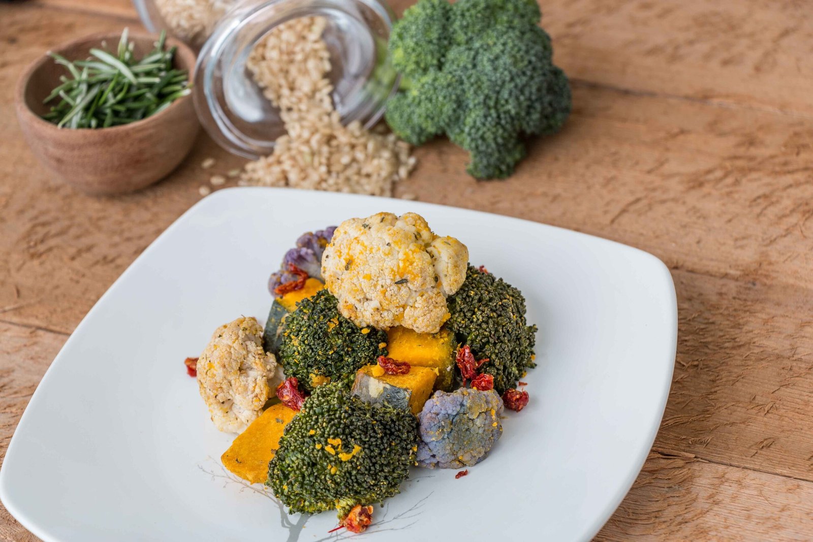 Close-up of a colorful roasted vegetable medley on a white plate with ingredients in background.